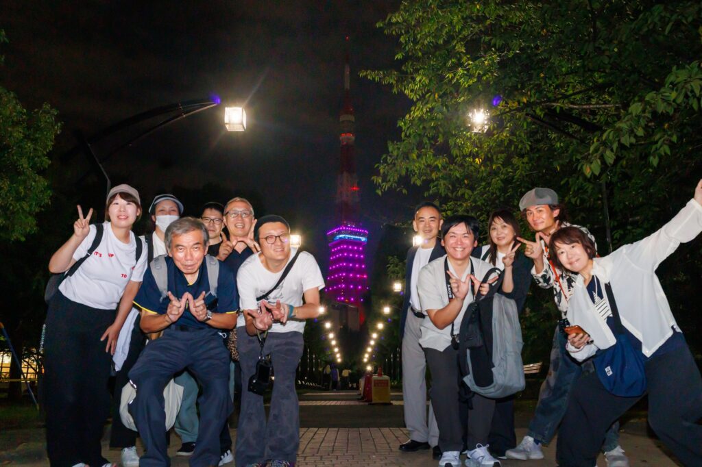 芝公園の並木道で、ライトアップされた東京タワーを背景にポーズをとるTokyo WordPress Meetupフォトウォークの参加者たち